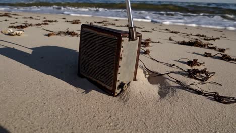 radio vintage descansando en la playa de arena, rodeado de algas esparcidas, con suaves olas del océano golpeando la costa bajo un vasto cielo azul claro