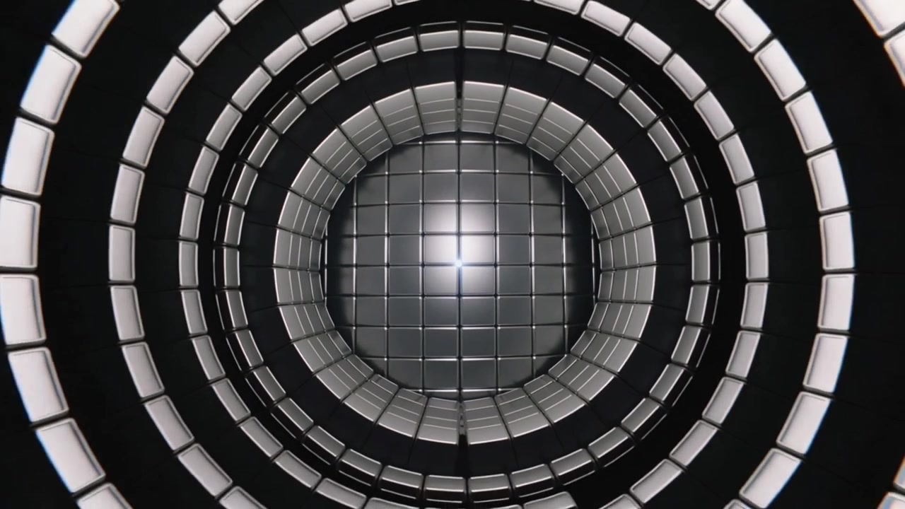La telecamera si allontana rivelando anelli cilindrici concentrici piastrellati nel vuoto, piastrelle metalliche e un bagliore centrale luminoso.