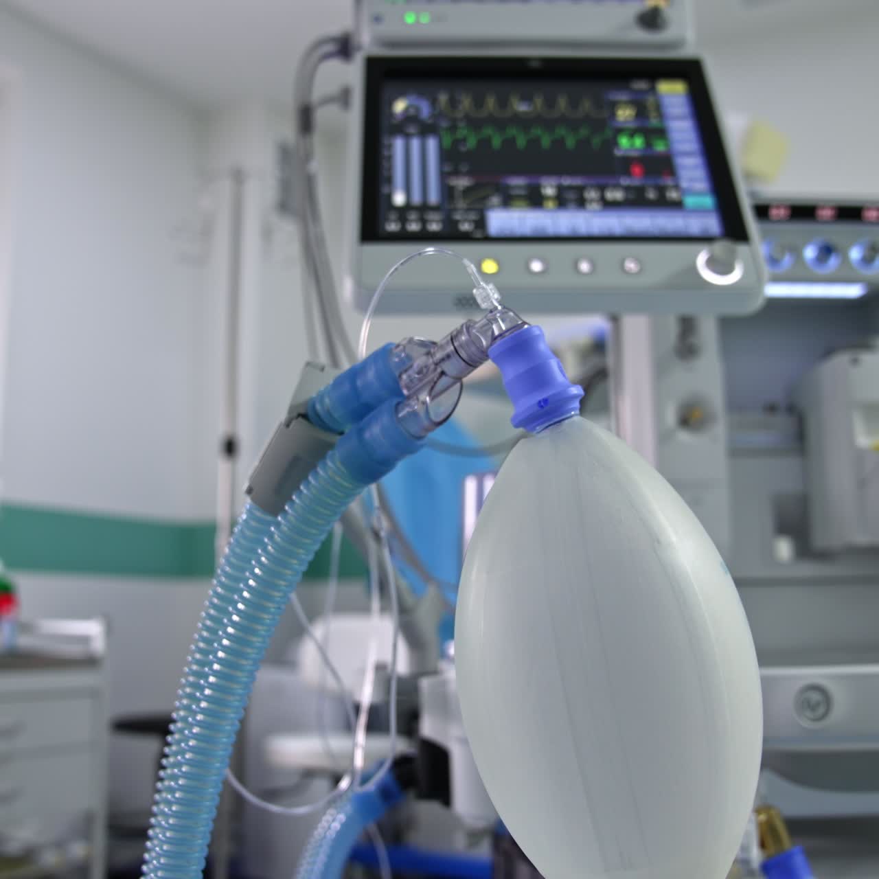 Inflating ambu bag hanging in the surgery room. Screen with life signs from a lung ventilator machine at backdrop in blur
