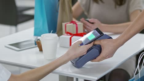 mujer pagando con teléfono inteligente en un café