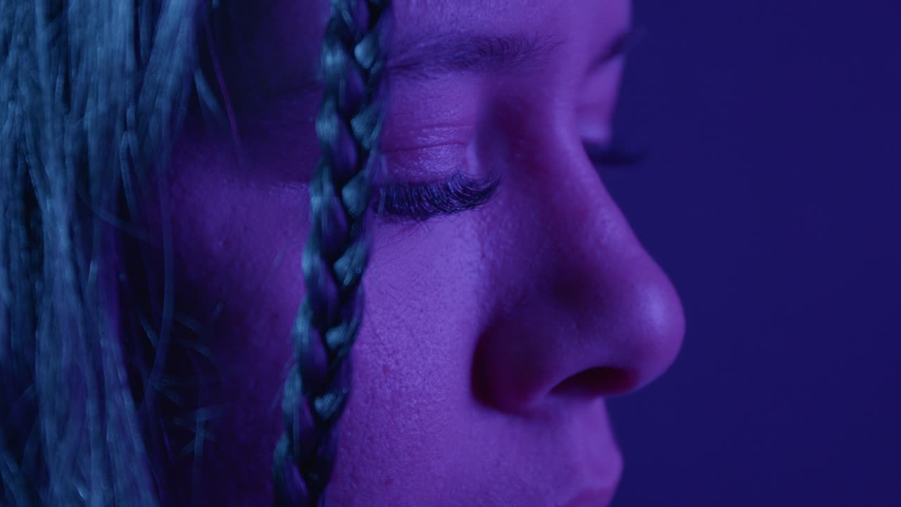 A captivating close-up shot of a girl with braided hair under ethereal purple lighting, highlighting her closed eyes. The soft focus and vibrant colors create an introspective mood