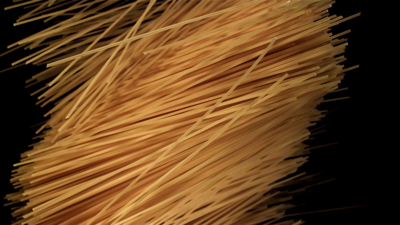Spaghetti secchi che cadono al rallentatore su sfondo nero