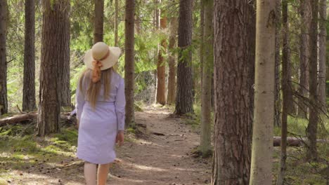 blond young woman walking the forest road in casual purple dress