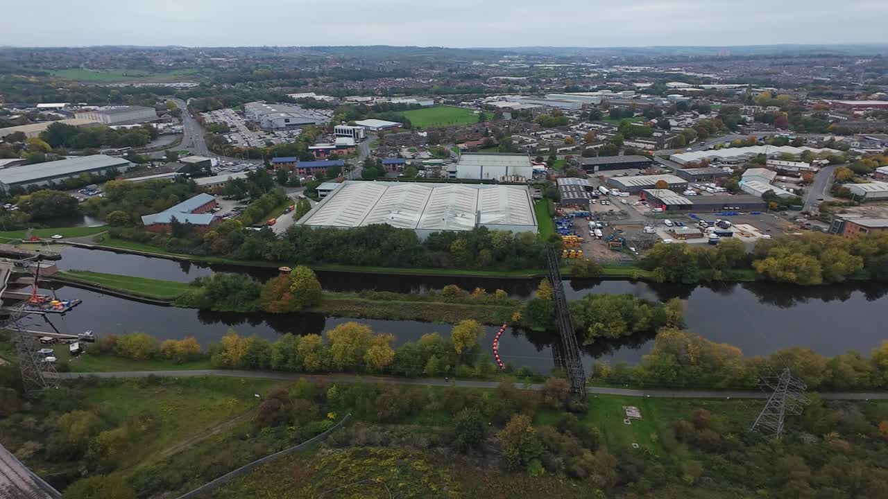 Leeds'in nehir ve sanayi bölgesinin havadan görüntüsü; bulutlu bir panoramada depolar, demiryolu, nehir kıvrımı ve yeşil kıyılar ile dağınık yollar, yavaş trafik, bağlama noktaları ve sakinleştirici sulak alanlar görülüyor.
