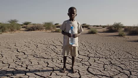 hopeful african child standing on dry, cracked earth, clutching a plastic bottle of clean water, symbolizing the struggle for survival amidst drought and climate change