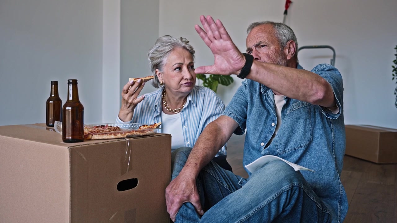 Coppia anziana felice che mangia pizza e parla nella nuova casa