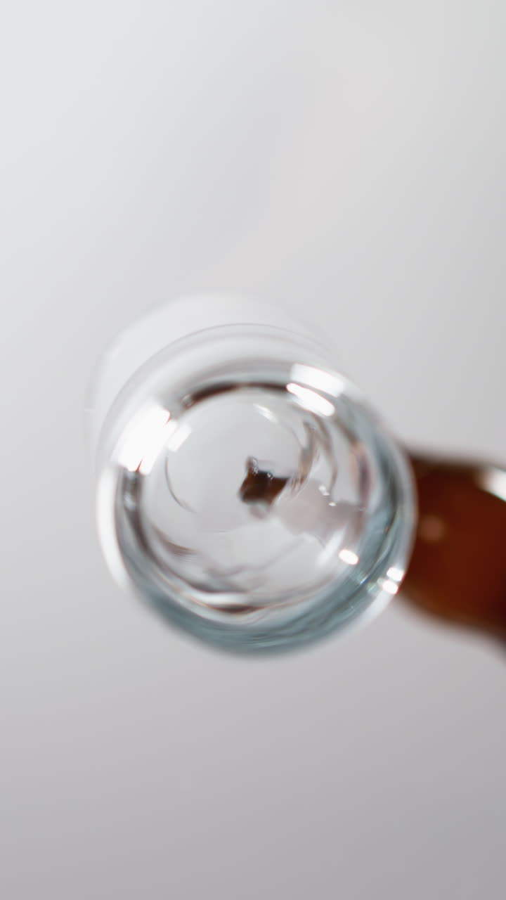 macro disparo de líquido transparente girando en una botella de vidrio sostenida por una mano femenina contra un fondo gris