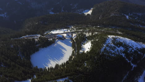 aerial shot closing in to a frozen black forest lake and hotel, are only partly snow covered, golden hour morning light