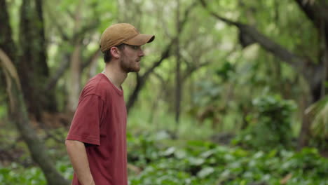 cinematic follow video of a young and fashionable man running through a large, green and overgrown forest in the middle of the hawaiian countryside