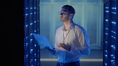ingeniero de red masculino haciendo una comprobación de sistema de pie en la sala de servidores con su computadora portátil. en el centro de datos hombres especialistas en servidores inspeccionando el sistema de trabajo y el hardware de los gabinetes de computadoras de servidor de rack