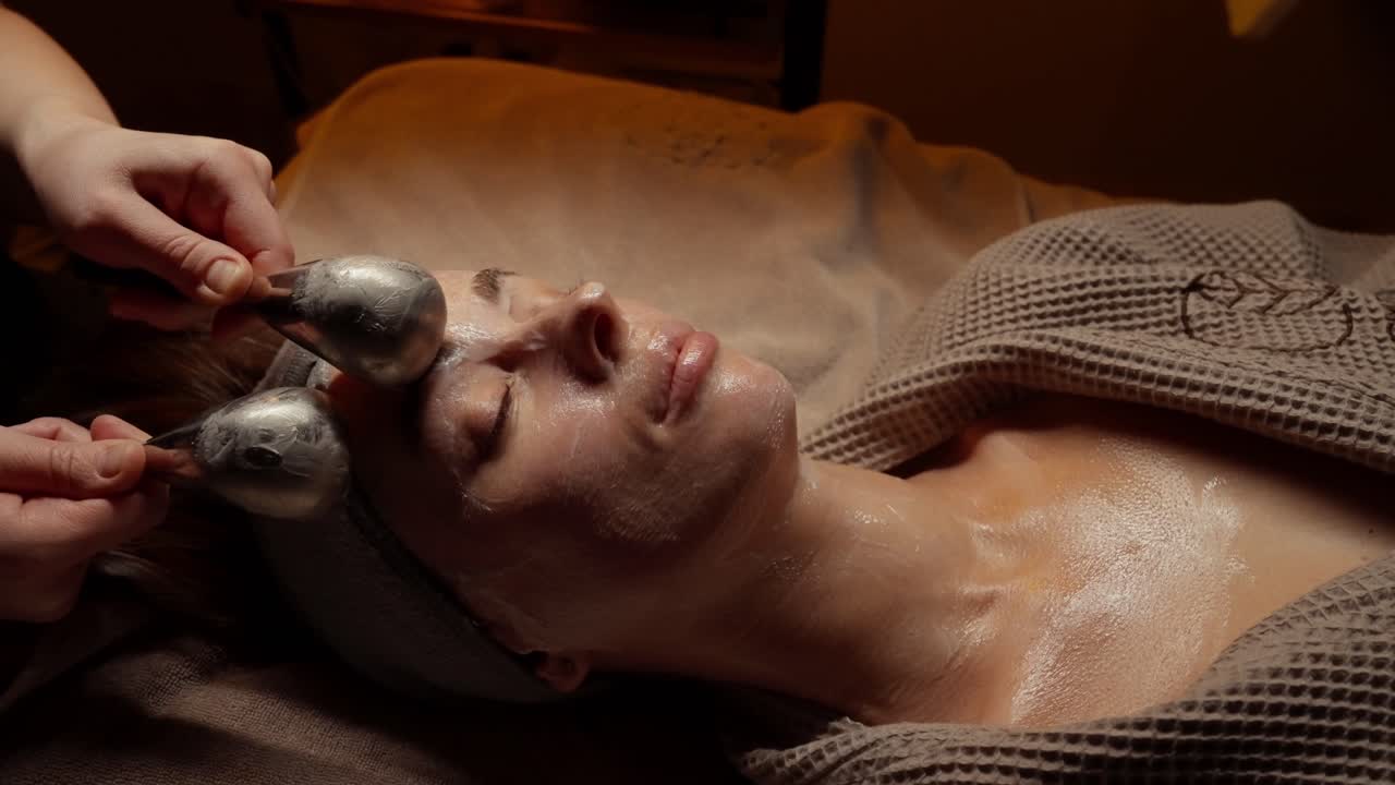 Kvinde får afslappende ansigtsmassage med iskugler i spa