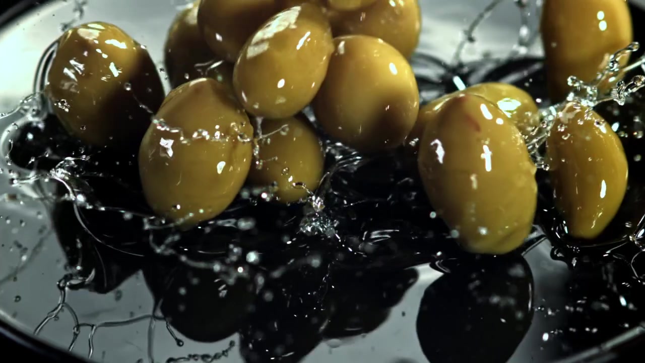 Olive verdi che cadono e schizzano nel liquido al rallentatore