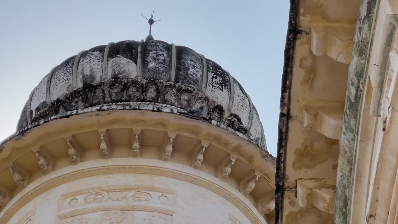 A weathered dome with darkened stone patterns and carved details stands against a clear sky, showcasing the aged beauty of historic Indian architecture