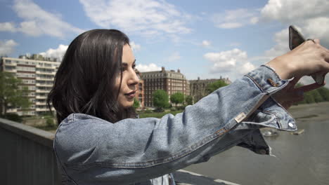 attractive hispanic tourist taking a picture of london from a bridge, taking her phone out and holding it to frame the shot