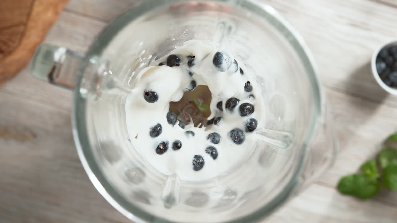 йогуртный коктейль из голубой ягоды с мятой, смешанный в стеклянном блендере в замедленном движении, вид сверху, внутри устройства