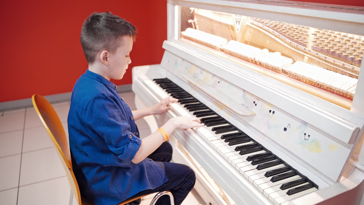 Side view of a child playing the white piano. Young boy learns how to play the piano. Piano lessons. Kid and musical instrument. Musical education. Hobbies.