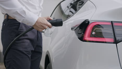 tesla driver puts the charging plug into the charging port of his tesla