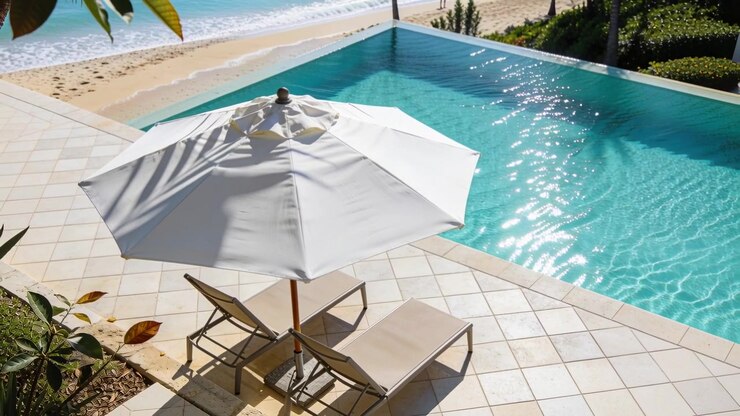 Shifting sun glinting on blue pool by white umbrella, lounge chairs on patio, walkers strolling