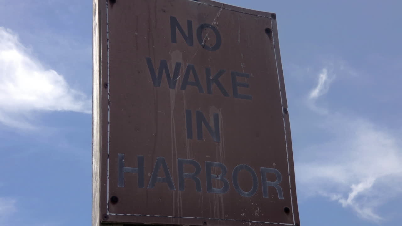 Pan up of old, weathered No Wake in Harbor sign