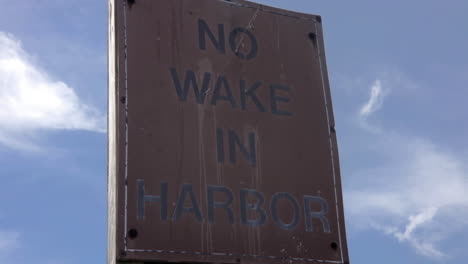 pan up of old, weathered no wake in harbor sign