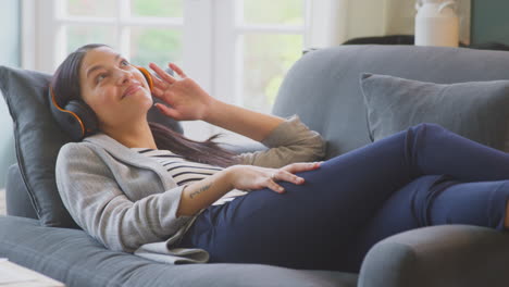 woman working from home taking a break lying on sofa listening to music on wireless headphones