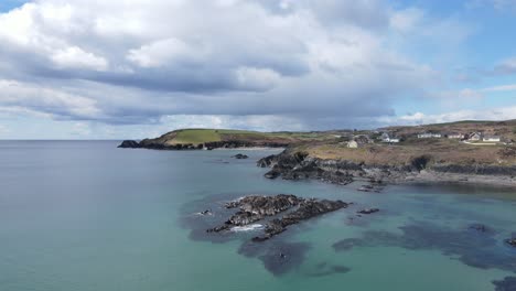 wide aerial footage flying backwards over green blue waters of calm sunny atlantic, rugged coastal line and dramatic sky in ireland