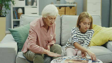 grandmother and her pretty teen granddaughter putting together puzzles while sitting on the sofa at home