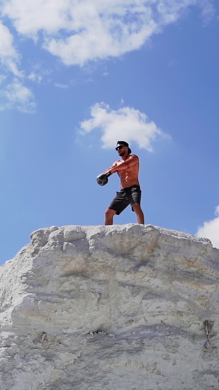 Fitness training man lifting heavy kettlebell weight. Muscular man lifts weight on the top of high hill. Cross training outdoors. Vertical video