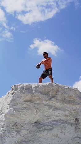 fitness training man lifting heavy kettlebell weight. muscular man lifts weight on the top of high hill. cross training outdoors. vertical video