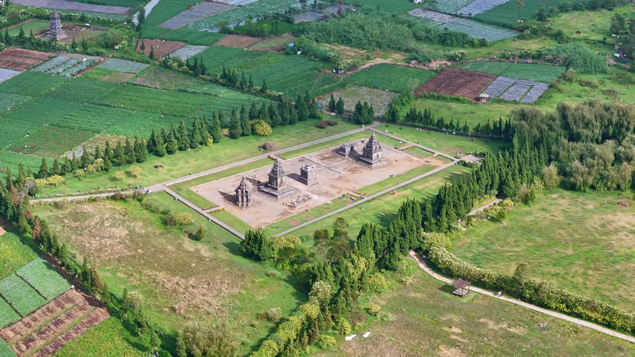 Drone view of ancient Hindu temples at Arjuna Temple complex, Dieng Plateau, with scenic farmlands and lush greenery in the background
