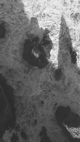 scenic morning aerial drone shot of praia da ursa’s rocky cliffs near cabo da roca, portugal. vertical video. black and white