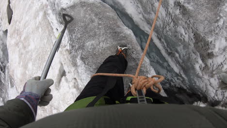 Feet-of-a-mountaineer-walking-on-a-glacier,-he-crosses-a-deep-crevasse,-equipped-with-crampons-and-rope,-ice-axe,-switzerland