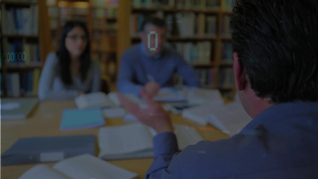 Istruttore che alza la mano per indicare un punto su un tavolo di legno mentre guida una sessione di studio con libri aperti