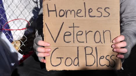 homeless veteran being interviewed and talking with his hands while holding sign saying, "homeless veteran, god bless"