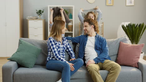 Young-Parents-Sitting-On-The-Sofa-In-The-Living-Room-And-Their-Funny-Cheerful-Kids-Beating-Them-With-Pillows