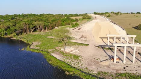 Volando-Hacia-La-Construcción-De-Una-Carretera-Y-Un-Puente-Que-Atravesará-Un-Sitio-De-Conservación-Del-Suelo-De-Un-Estanque