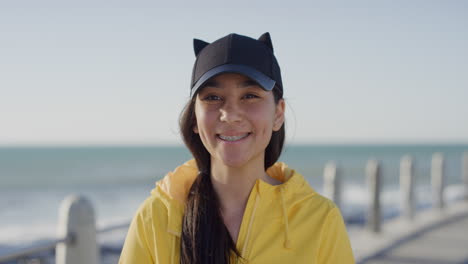 Retrato-De-Una-Adolescente-De-Raza-Mixta-Sonriendo-Alegre-Mirando-La-Cámara-Usando-Una-Chaqueta-Amarilla-Disfrutando-De-La-Soleada-Playa-Junto-Al-Mar