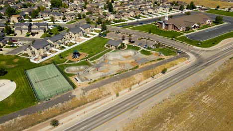 Orbiting-aerial-view-of-an-urban-skate-park-between-a-highway-and-a-suburb