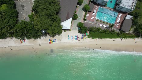 A vibrant aerial elevator shot looking down on colourful surfboards and a pristine beach on Koh Phi Phi, Thailand.