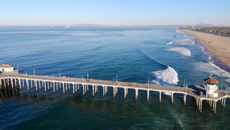 wide fly in to huntington beach pier, lifeguard tower, and surfers with aerial 4k drone at early morning on pacific ocean on southern california coastline