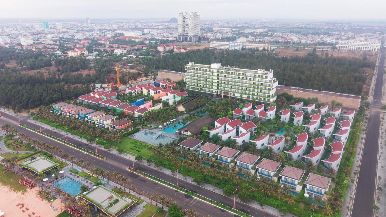 Khám phá Bãi biển Tuy Hòa ở Việt Nam, nơi mọi người thư giãn trên bờ. Ngắm nhìn mặt trời chiếu sáng trên mặt nước và du khách tận hưởng các hoạt động trên bãi biển. Nhiều tòa nhà dọc theo bờ biển.