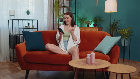 retrato de una niña adulta sentada en el sofá, usando un teléfono inteligente para compartir mensajes en aplicaciones de redes sociales