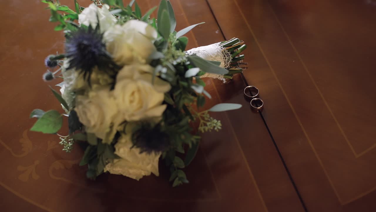 Wedding rings lie near beautiful wedding bouquet on the wooden table