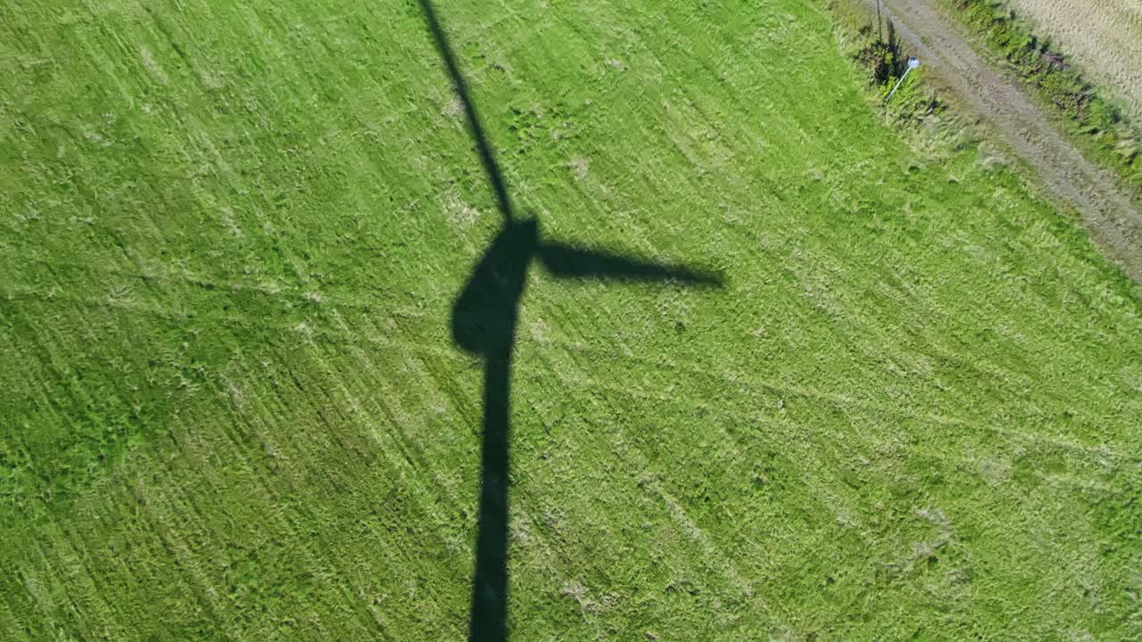 Shadow of wind turbine spinning slowly over a green summer field, aerial top view