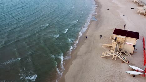 plano largo aéreo sigue a un hombre corriendo en la playa, puesto de salvavidas, disparo de un dron