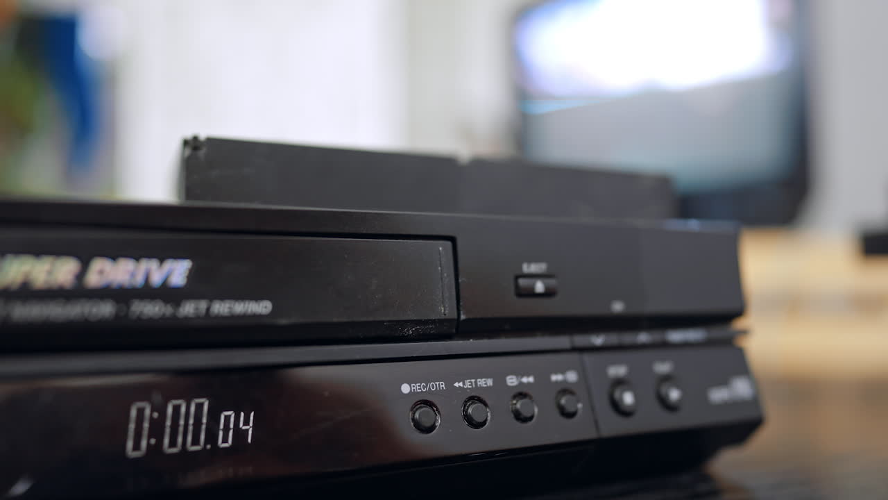 Un dito preme il pulsante di controllo del videoregistratore. Una mano in primo piano preme un pulsante su un vecchio videoregistratore con una TV sfocata sullo sfondo