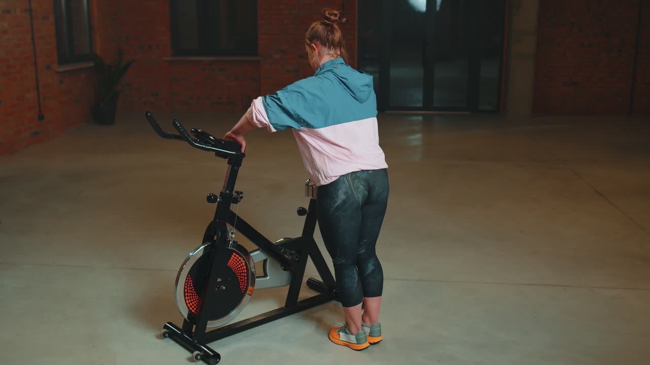 운동하는 소녀는 자전거에서 아크로바틱 트릭을 하고 실내에서 정지 자전거 기계에서 운동을 합니다.