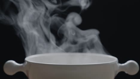 the hot tea in the white cup has white smoke and steam effect on the black background.