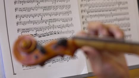 primer plano de una talentosa mujer violinista, profundamente en la práctica, con una hoja de notas musicales borrosa en el fondo