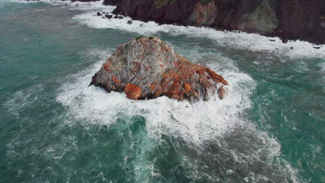 scoglio il morto, sardinia, iglesias: aerial view in orbit over the famous islet and the waves hitting the rock hard